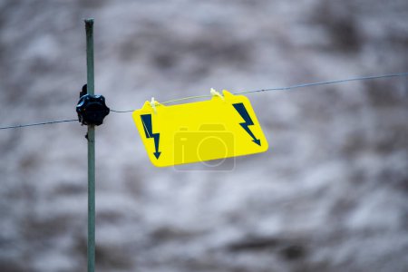 Photo for Electric fence warning sign. A yellow warning sign hangs on a wire and warns of danger - Royalty Free Image