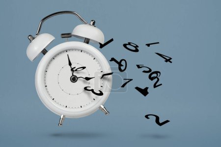 Téléchargez les photos : Le temps presse. Réveil blanc avec numéros volants comme symbole du temps perdu. Le concept de temps s'épuise, la perte ou le manque de temps, un réveil avec des chiffres se brise en petits morceaux - en image libre de droit