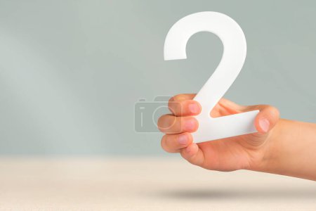 Nummer zwei in der Hand. Hand hält weiße Zahl 2 auf verschwommenem Hintergrund mit Kopierraum. Konzept mit Nummer zwei. 2 Prozent, Geburtstag 2 Jahre alt, Paar, zwei, zwei.