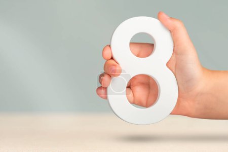 Eight in hand. A hand holds a white number 8 on a blurred background. Concept with number eight. Birthday 8 years, percentage, eighth grade or day, international womens day