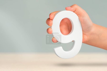 Number nine in hand. A hand holds a white number 9 on a blurred background. Concept with number nine. Birthday 9 years, percentage, ninth grade or day