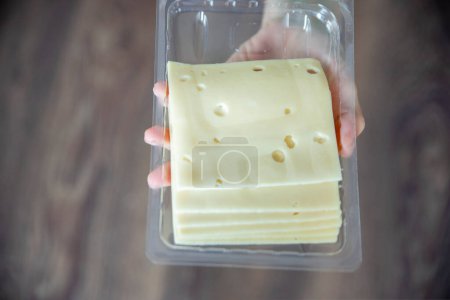 Téléchargez les photos : Une main de femme prend un morceau de fromage d'un paquet gros plan. Préparation pour la journée des amateurs de fromage. Photo de haute qualité - en image libre de droit