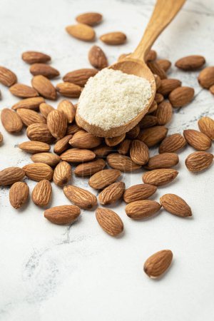 Photo for Wooden spoon full of almond flour on dried almond seeds. Almonds on the white marble background. Ingredient for French dessert macaroons. Healthy nutrition concept. Flat lay - Royalty Free Image