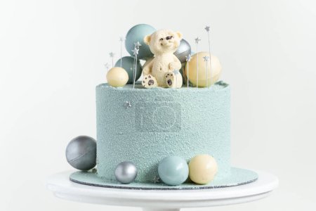 Kuchen in blauem oder türkisfarbenem Samt mit Teddybär an der Spitze. Geburtstagstorte für ein kleines Baby mit Schokotürkis und silbernen Kugeln auf weißem Hintergrund. Ein Jahr Feier.
