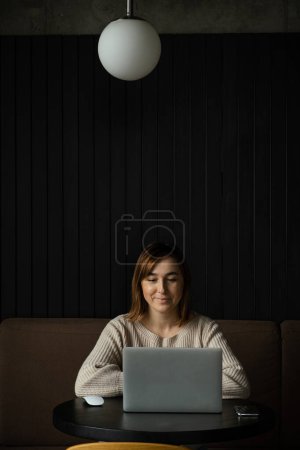 Photo for Beautiful happy caucasian woman using laptop in a modern workspace. Cute dreamy young business woman sitting at a table in a restaurant - Royalty Free Image