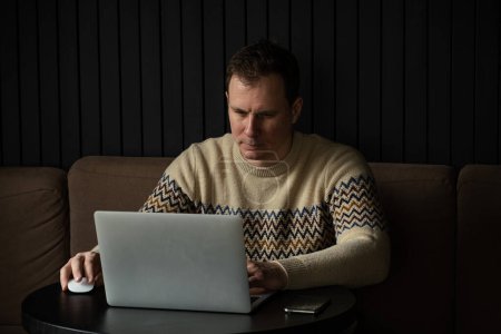 Photo for Young caucasian man concentrated using laptop in a modern workspace.  Successful freelancer focused while writing letter and typing on a keyboard - Royalty Free Image