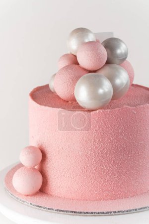 Birthday cake with pink velvet sprayed coating decorated with silver and pink chocolate spheres on the white background