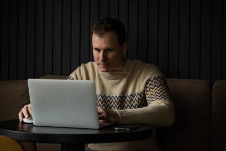 Photo for Young caucasian man concentrated using laptop in a modern workspace.  Successful freelancer focused while writing letter and typing on a keyboard - Royalty Free Image