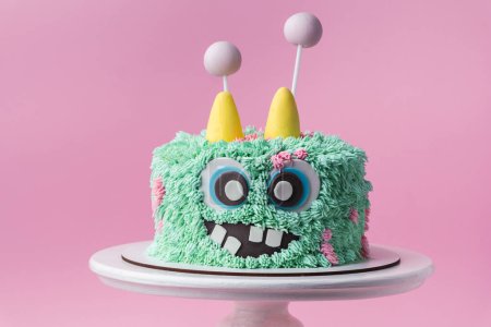 Monster Thema Kuchen auf dem rosa Hintergrund. Lustige Geburtstagstorte mit türkisfarbenem flauschigem Frischkäse-Zuckerguss. Gespenstisches Monstergebäck mit essbarem Fell. Fröhliche Halloween-Party