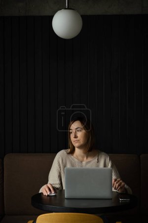 Photo for Beautiful happy caucasian woman using laptop in a modern workspace. Cute dreamy young business woman sitting at a table in a restaurant - Royalty Free Image