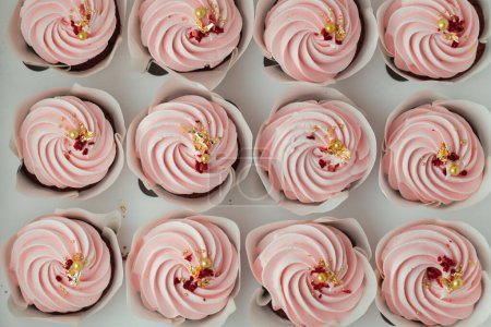 Photo for Set of cupcakes with pink whipped cream top decorated with edible golden petals and red dried berries. Close-up shot of cupcakes in the white background. Top view - Royalty Free Image
