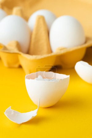 Großaufnahme weißer Eier in der braunen Schachtel auf gelbem Hintergrund. Makroaufnahme eines zerbrochenen Eies mit weißer Schale. Kopierplatz für einen freien Text.