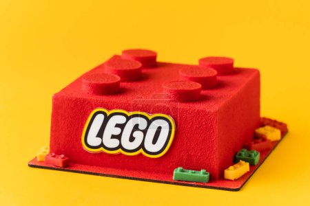 Foto de KYIV, UCRANIA - 11 de octubre: Tarta de Lego de cumpleaños en forma de ladrillo lego rojo rociado con recubrimiento de terciopelo de chocolate sobre el fondo amarillo. - Imagen libre de derechos