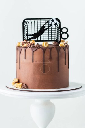 Foto de Tarta de cumpleaños para un fanático del fútbol con glaseado de queso crema marrón y gotas de chocolate decoradas con silueta de portero aborda la pelota. - Imagen libre de derechos