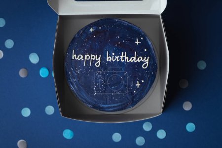 Photo for Birthday little cake with blue cream cheese frosting decorated with happy birthday text on top. Trendy bento cake in the white gift box on the dark blue background surrounded with confetti. Flat lay - Royalty Free Image
