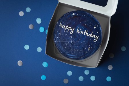 Photo for Birthday little cake with blue cream cheese frosting decorated with happy birthday text on top. Trendy bento cake in the white gift box on the dark blue background surrounded with confetti. Flat lay - Royalty Free Image
