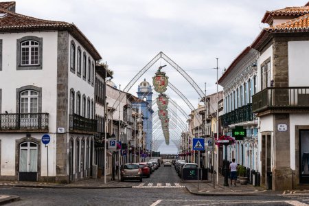 Foto de Angra do Heroismo, Portugal - 3 de julio de 2022: Calle comercial adornada con arcos de acero y escudos colgantes en el casco antiguo de Angra do Heroismo. Isla Terceira, Azores. - Imagen libre de derechos
