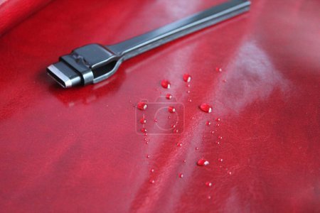 Red natural leather with water droplets, on which is a tool designed for working with leather - a chisel for the production of leather goods.