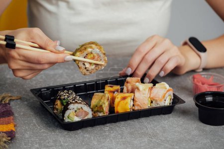 Téléchargez les photos : Gros plan sur la cuisine japonaise à emporter. Femme mangeant un rouleau de sushi à l'aide de baguettes d'un récipient en plastique - en image libre de droit