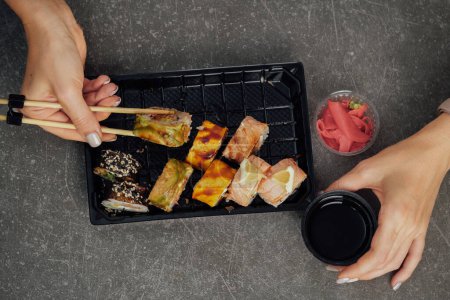 Téléchargez les photos : Gros plan sur la cuisine japonaise à emporter. Femme mangeant un rouleau de sushi à l'aide de baguettes d'un récipient en plastique - en image libre de droit