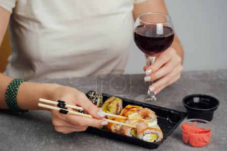 Téléchargez les photos : Gros plan sur la nourriture de rue japonaise. Femme mangeant un rouleau de sushi en utilisant des baguettes et boire du vin - en image libre de droit