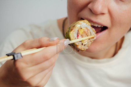 Téléchargez les photos : Femme apporte rouleau de sushi en utilisant des baguettes à sa bouche et aime la nourriture japonaise - en image libre de droit