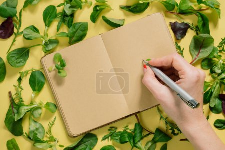 Téléchargez les photos : Pages blanches du carnet près des feuilles vertes et des ingrédients alimentaires pour la recette de cuisson. Vue du dessus avec espace de copie sur fond jaune pour le texte - en image libre de droit