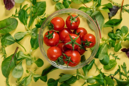 Téléchargez les photos : Vue de dessus des tomates cerises, entourées de feuilles vertes fraîches sur une table. Les ingrédients sains peuvent être utilisés dans diverses recettes alimentaires naturelles - en image libre de droit