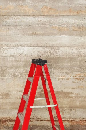 Photo for Red folding ladder on concrete cement textured wall for background - Royalty Free Image