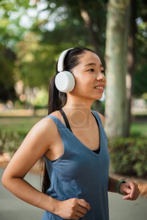 Photo for Asian sport girl running in the park while she is listening to music on wireless headphones - Royalty Free Image