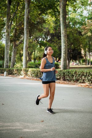 Photo for Fitness young woman jogging in the park while she is listening to music on wireless headphones - Royalty Free Image