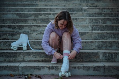 Téléchargez les photos : Jeune femme attachant les lacets de ses patins à roulettes tout en étant assis sur les escaliers - en image libre de droit