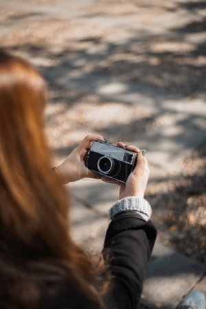 Photo for Young woman taking a selfie using an old analog camera on a bench. - Royalty Free Image
