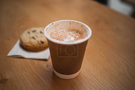 Téléchargez les photos : Gros plan d'une tasse de cappuccino chaud avec un biscuit au chocolat sur une table d'un café - en image libre de droit