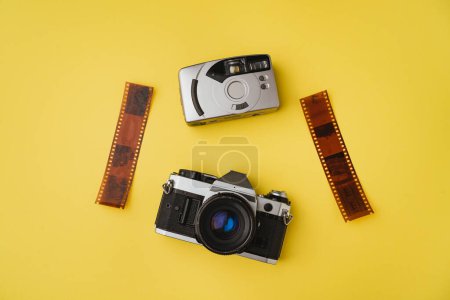 Foto de Vista de ángulo alto de dos cámaras de película retro con negativos sobre fondo amarillo - Imagen libre de derechos