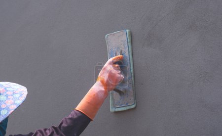 Téléchargez les photos : Gros plan de la main ouvrière de la construction dans le mur de ciment de polissage à gants en caoutchouc, vue latérale perspective avec espace de copie - en image libre de droit