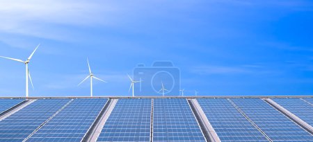 Téléchargez les photos : Vue panoramique de nombreux panneaux solaires photovoltaïques sur le toit de construction d'usine avec éoliennes sur fond bleu, concept d'énergie durable et renouvelable - en image libre de droit