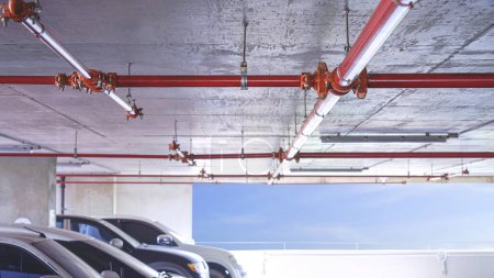 Foto de Sistema de tubería de agua protectora contra incendios rojo en el techo de hormigón dentro del edificio de garaje de estacionamiento, enfoque selectivo - Imagen libre de derechos