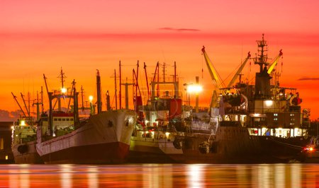 Group of fishing boats and oil tanker ship dock at harbor in industrial riverside area against beautiful dramatic twilight sky background