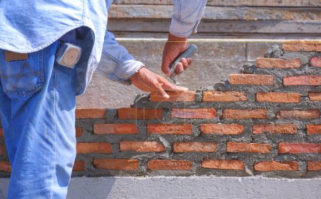 Nahaufnahme von Bauarbeiterhänden macht niedrige Mauer aus Ziegelstein in Hausbaustelle
