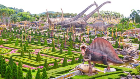 Foto de Chonburi, Tailandia - 24 de septiembre de 2023: Grupo de grandes estatuas de dinosaurios con hermoso jardín topiario en la maravillosa zona del valle tropical del jardín Nong Nooch en Pattaya, Tailandia - Imagen libre de derechos
