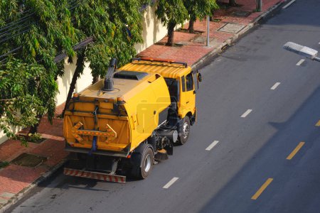 Téléchargez les photos : Balayeuse jaune nettoie dans la rue de la ville le matin, vue grand angle depuis le bâtiment - en image libre de droit