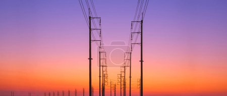 Silueta dos filas de postes eléctricos con líneas de cable en la carretera curva contra el colorido crepúsculo cielo fondo en vista panorámica