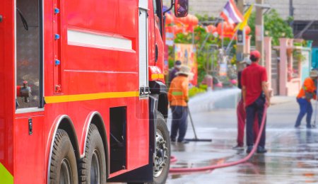 Focus at red fire truck with blurred background of cleaner workers group are cleaning street surface during the issue of airborne dust levels exceeding international standards