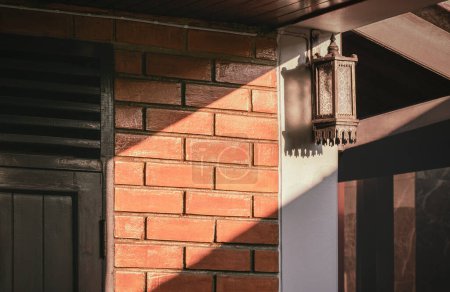 Foto de Luz solar y sombra en la superficie de la antigua lámpara de pared retro en la pared de madera de ladrillo y teca de la casa vintage - Imagen libre de derechos