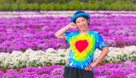 Foto de Turista asiática con camiseta arco iris sonríe alegremente y mira a la cámara mientras posa en floreciente campo de buganvillas rosa y blanca en el jardín tropical de Nong Nooch, Tailandia - Imagen libre de derechos