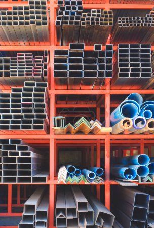 Varios tamaños de muchos tubos rectangulares y cuadrados de acero al carbono con tuberías de agua de PVC azul en el estante de almacenamiento de la tienda de suministro de edificios en marco vertical
