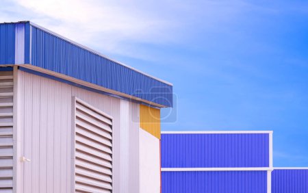 Foto de Ventana de aluminio en pared de almacén de acero corrugado con edificio de metal azul en el área de fábrica contra fondo de cielo azul - Imagen libre de derechos