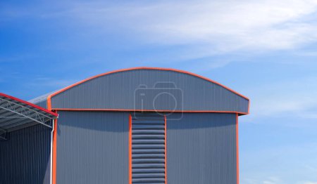 Large gray aluminium industrial warehouse building with curve roof next to pavilion against blue sky background