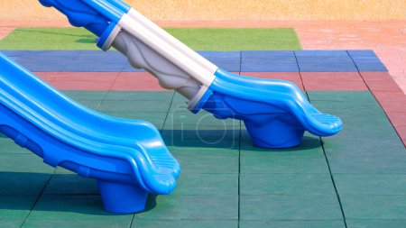 Partie de 2 toboggans sur tapis de sol en caoutchouc coloré EPDM avec gazon et carrelage en pierre dans l'aire de jeux extérieure publique